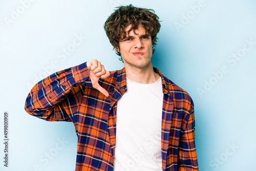 Young caucasian man isolated on blue background showing thumb down, disappointment concept.