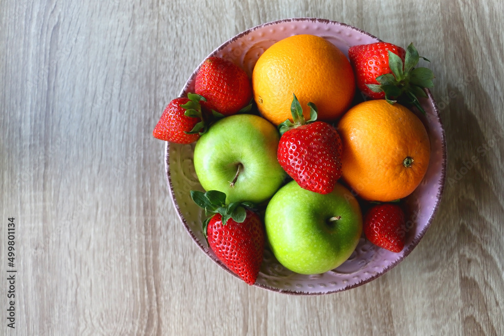 Pink bowl filled with fresh apples, oranges and strawberries on wooden table. Flat lay. Pink bowl filled with fresh apples, oranges and strawberries on wooden table. Flat lay.