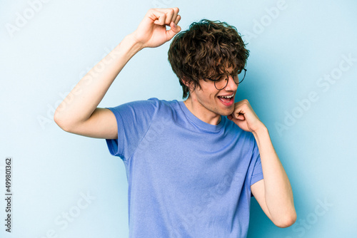 Young caucasian man isolated on blue background celebrating a special day, jumps and raise arms with energy.