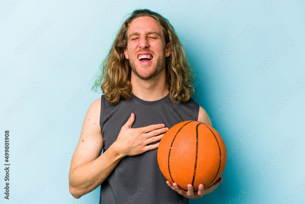 Young caucasian man playing basketball isolated on blue background laughs out loudly keeping hand on chest. Young caucasian man playing basketball isolated on blue background laughs out loudly keeping hand on chest.