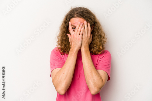Young caucasian man isolated on white background blink at the camera through fingers, embarrassed covering face. © Asier