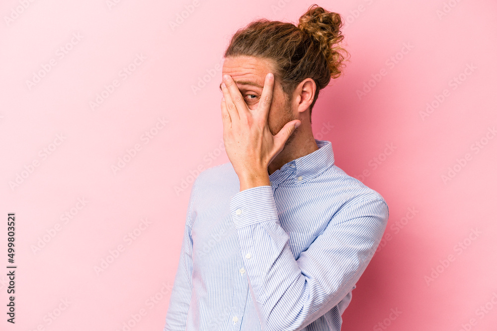 Young caucasian man isolated on pink background blink at the camera through fingers, embarrassed covering face. Young caucasian man isolated on pink background blink at the camera through fingers, embarrassed covering face.