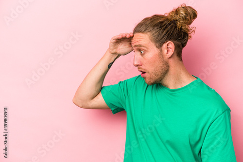 Young caucasian man isolated on pink background looking far away keeping hand on forehead.