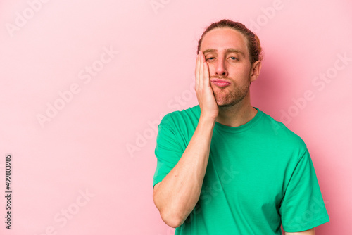 Young caucasian man isolated on pink background who feels sad and pensive, looking at copy space.