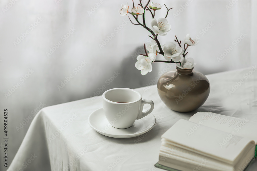 The atmosphere of a romantic spring morning. Blooming branches in a vase, a book and a cup of coffee on a white table in a Provence style garden. Home interior. Life style