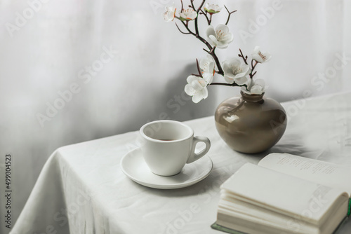 The atmosphere of a romantic spring morning. Blooming branches in a vase, a book and a cup of coffee on a white table in a Provence style garden. Home interior. Life style