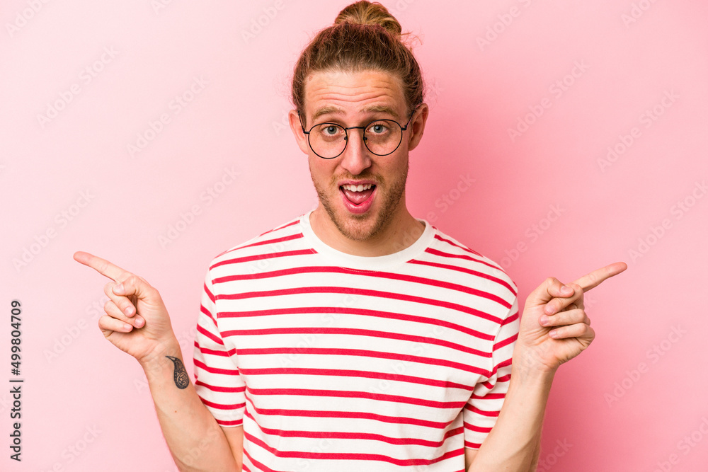 Young caucasian man isolated on pink background pointing to different copy spaces, choosing one of them, showing with finger. Young caucasian man isolated on pink background pointing to different copy spaces, choosing one of them, showing with finger.