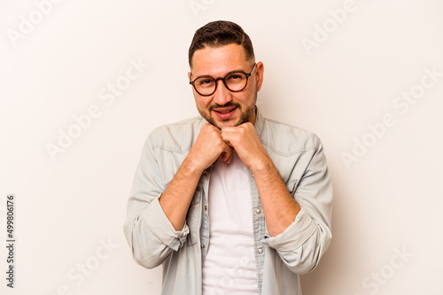 Young hispanic man isolated on white background keeps hands under chin, is looking happily aside.
