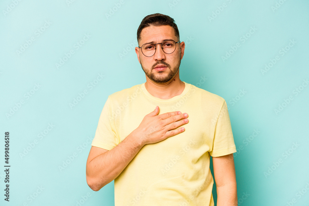 Young hispanic man isolated on blue background taking an oath, putting hand on chest. Young hispanic man isolated on blue background taking an oath, putting hand on chest.