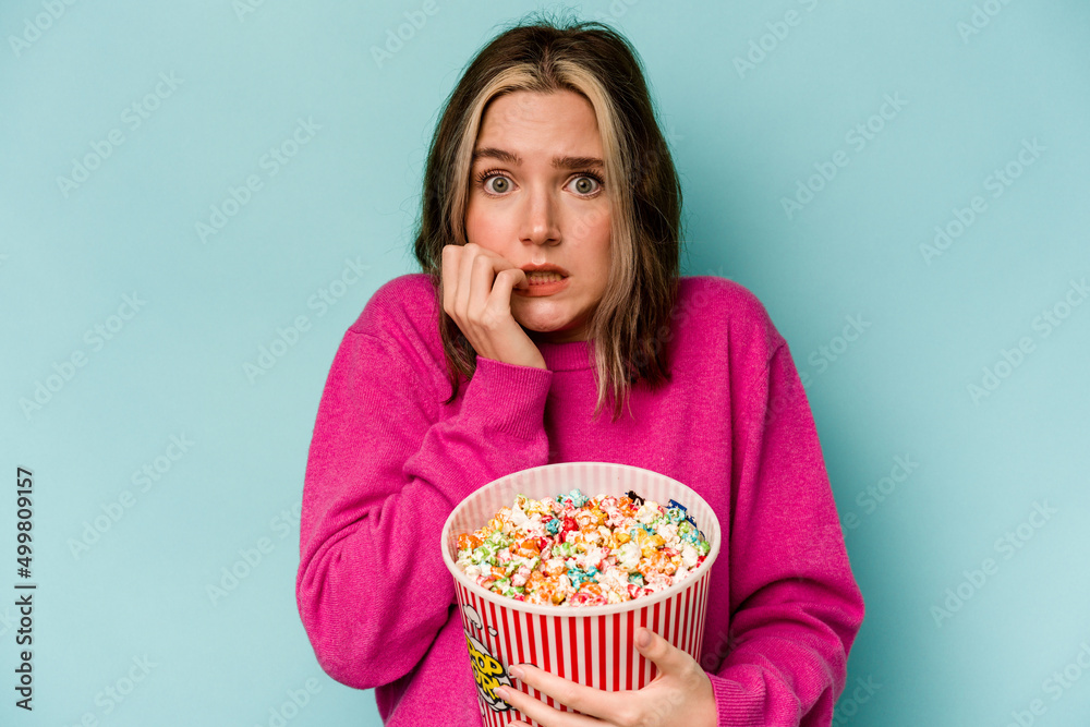Young caucasian woman holding popcorn isolated on blue background