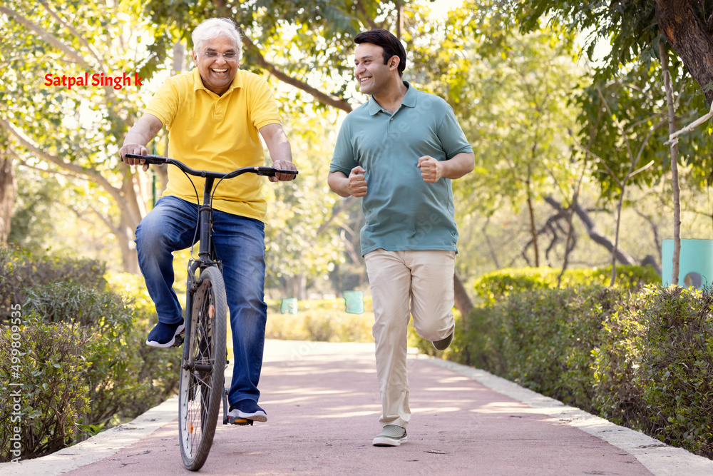 Cheerful senior man riding bicycle while son running at park Cheerful senior man riding bicycle while son running at park
