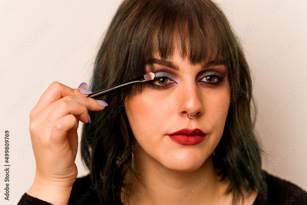 Young caucasian woman holding makeup brush isolated on pink background