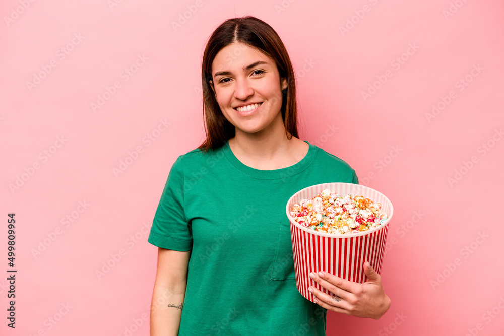 Young caucasian woman holding popcorn isolated on pink background happy, smiling and cheerful. Young caucasian woman holding popcorn isolated on pink background happy, smiling and cheerful.