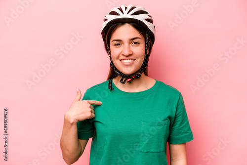 Young caucasian woman wearing helmet isolated on pink background person pointing by hand to a shirt copy space, proud and confident