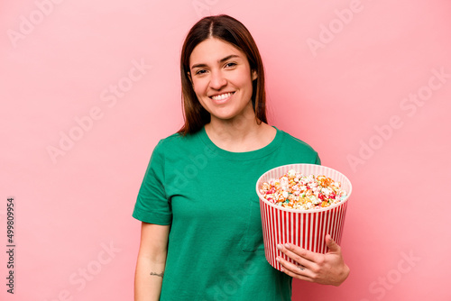 Young caucasian woman holding popcorn isolated on pink background happy, smiling and cheerful.