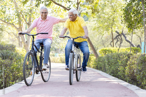 Two cheerful senior men having fun riding bicycle at park