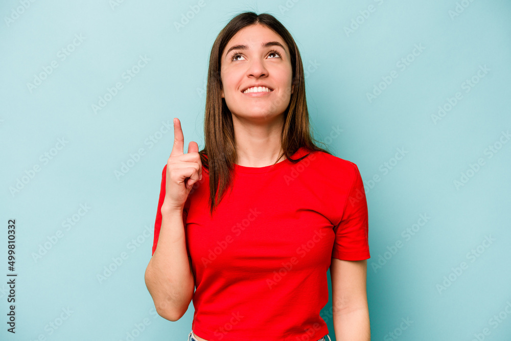 Young caucasian woman isolated on blue background indicates with both fore fingers up showing a blank space. Young caucasian woman isolated on blue background indicates with both fore fingers up showing a blank space.