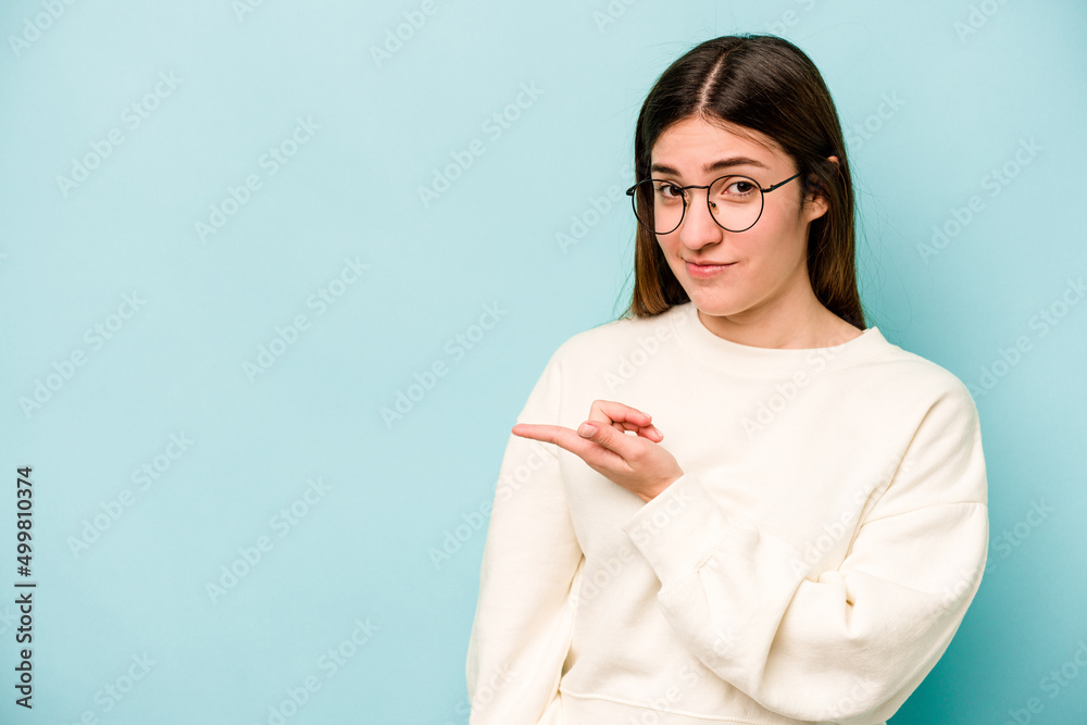 Young caucasian woman isolated on blue background smiling and pointing aside, showing something at blank space. Young caucasian woman isolated on blue background smiling and pointing aside, showing something at blank space.