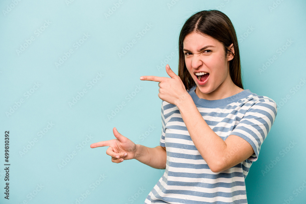 Young caucasian woman isolated on blue background pointing with forefingers to a copy space, expressing excitement and desire.