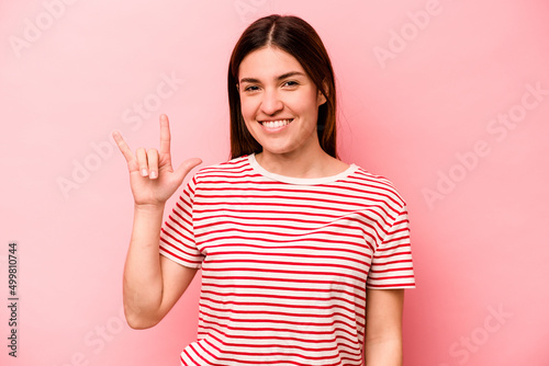 Young caucasian woman isolated on pink background showing a horns gesture as a revolution concept.