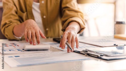 Close-up of business woman hands check company finance data reports and using calculator at desk in modern office.