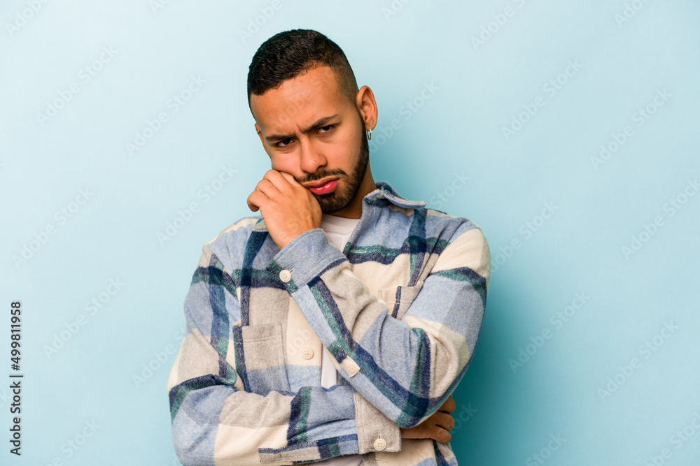 Young hispanic man isolated on blue background tired of a repetitive task. Young hispanic man isolated on blue background tired of a repetitive task.