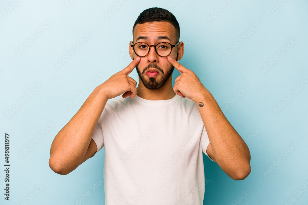 Young hispanic man isolated on blue background crying, unhappy with something, agony and confusion concept. Young hispanic man isolated on blue background crying, unhappy with something, agony and confusion concept.