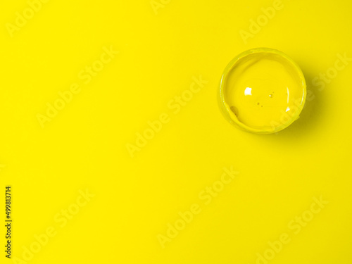 A jar of yellow paint on a yellow background. Bank of gouache. Bright background. Artist's workshop.