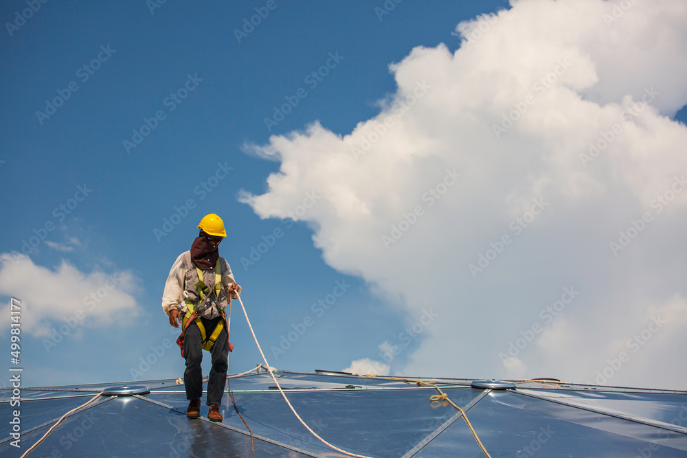 Male workers rope access height safety connecting with a knot safety harness, clipping into roof construction site oil tank dome Male workers rope access height safety connecting with a knot safety harness, clipping into roof construction site oil tank dome