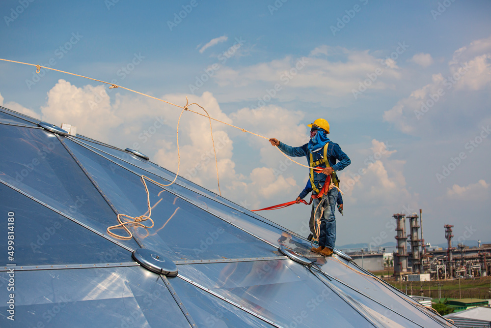 Male workers rope access height safety connecting with eight knots safety harness construction site oil tank dome. Male workers rope access height safety connecting with eight knots safety harness construction site oil tank dome.