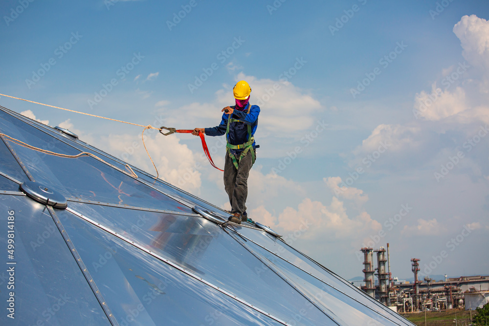 Male workers rope access height safety connecting with a knot safety harness, clipping into roof construction site oil tank dome Male workers rope access height safety connecting with a knot safety harness, clipping into roof construction site oil tank dome