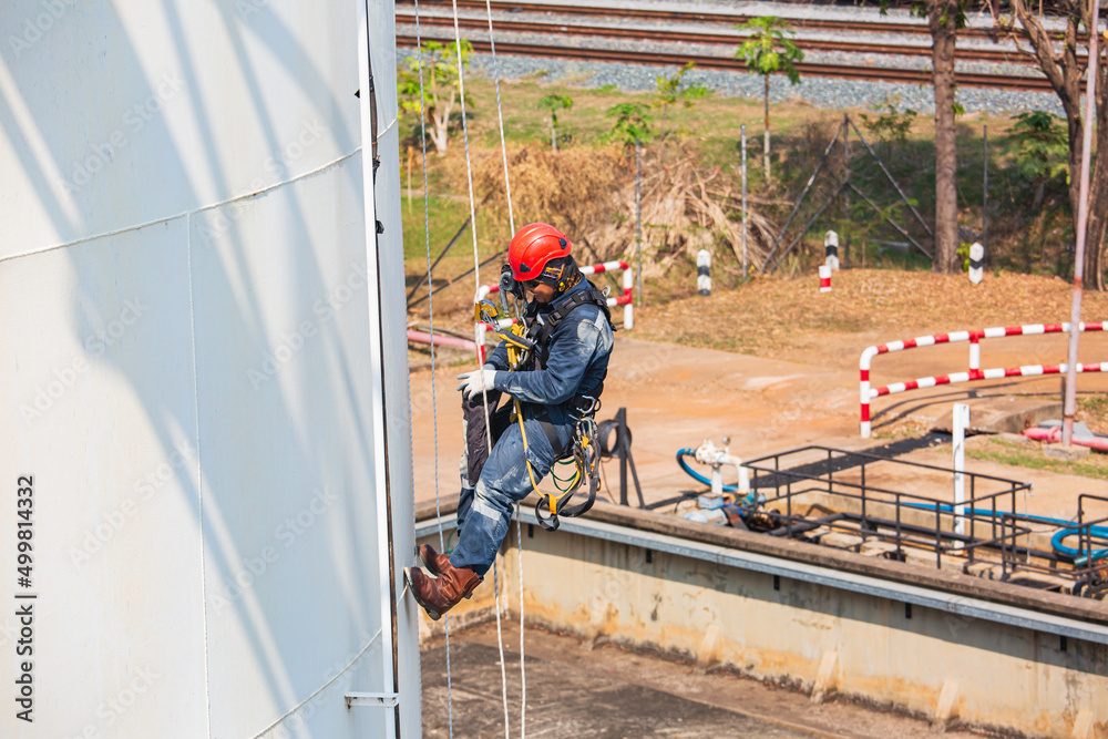 Top view pic of industrial rope access welder working at height wearing harness, helmet safety equipment rope access inspection of thickness storage tank Top view pic of industrial rope access welder working at height wearing harness, helmet safety equipment rope access inspection of thickness storage tank