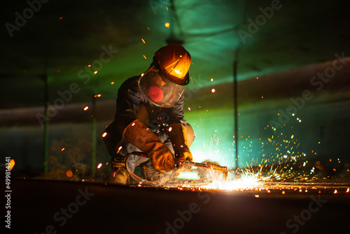 Male worker metal cutting spark on tank bottom steel plate with flash of cutting light close up wear protective gloves and mask