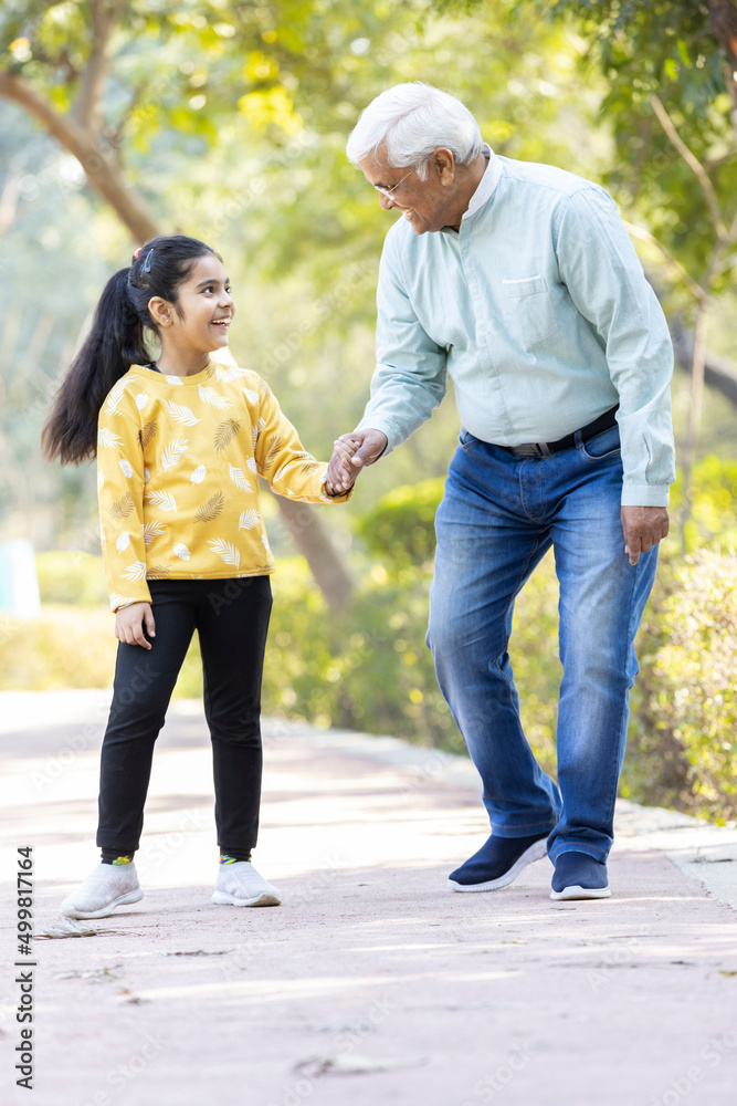 Obraz premium Senior man holding stick while walking with granddaughter at park