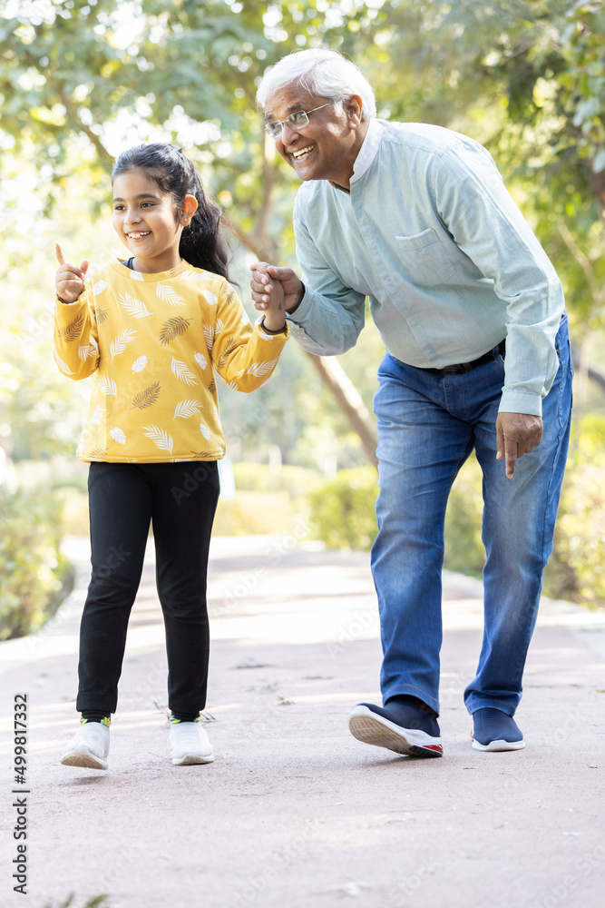 Obraz premium Senior man holding stick while walking with granddaughter at park