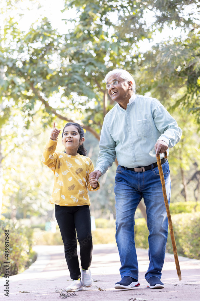 Senior man holding stick while walking with granddaughter at park Senior man holding stick while walking with granddaughter at park