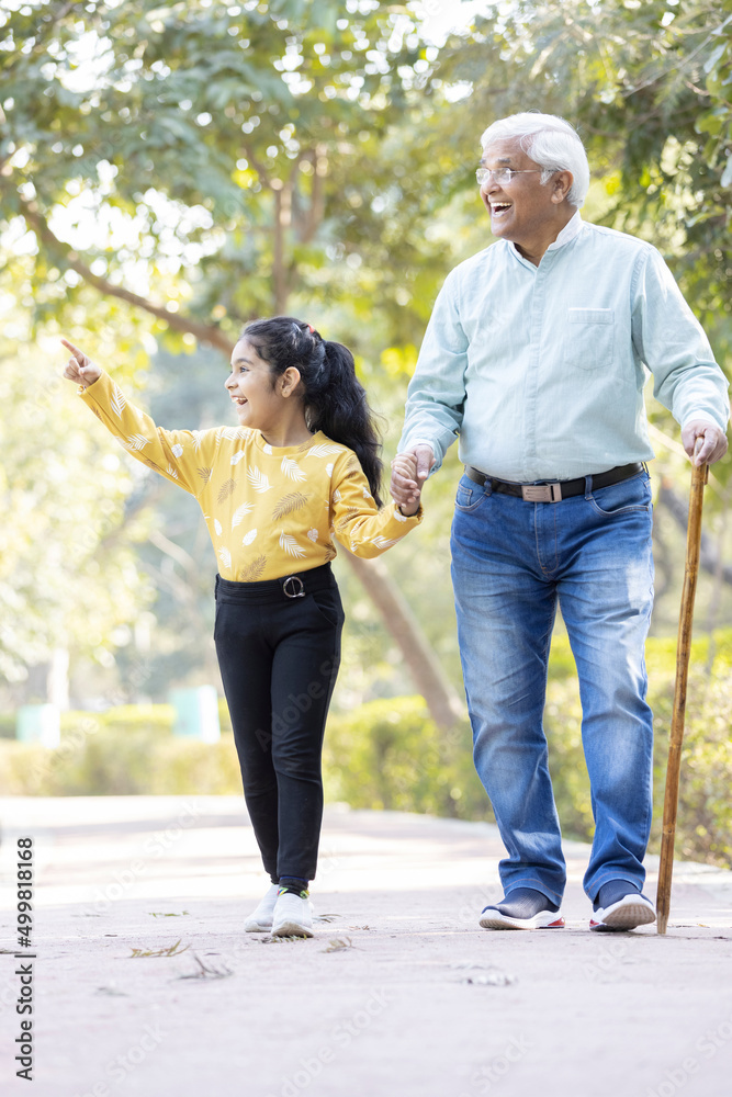 Senior man holding stick while walking with granddaughter at park Senior man holding stick while walking with granddaughter at park
