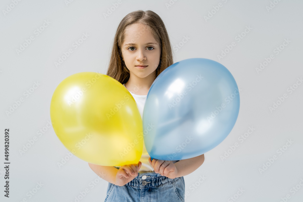 ukrainian girl holding blue and yellow balloons while looking at camera isolated on grey. ukrainian girl holding blue and yellow balloons while looking at camera isolated on grey.