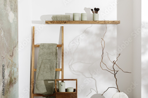 Modern aesthetic bathroom accessories in eucalyptus green shade. Organic cotton bath towels, sensor soap and lotion dispenser  on solid oak stump. Daily body care, spa and wellness  bathroom concept