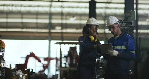 UntitleIndustrial engineer, technician worker wearing uniform, safety hard hat using tablet computer checking control automated robotic arm machine in factory. Automatic manufacturing