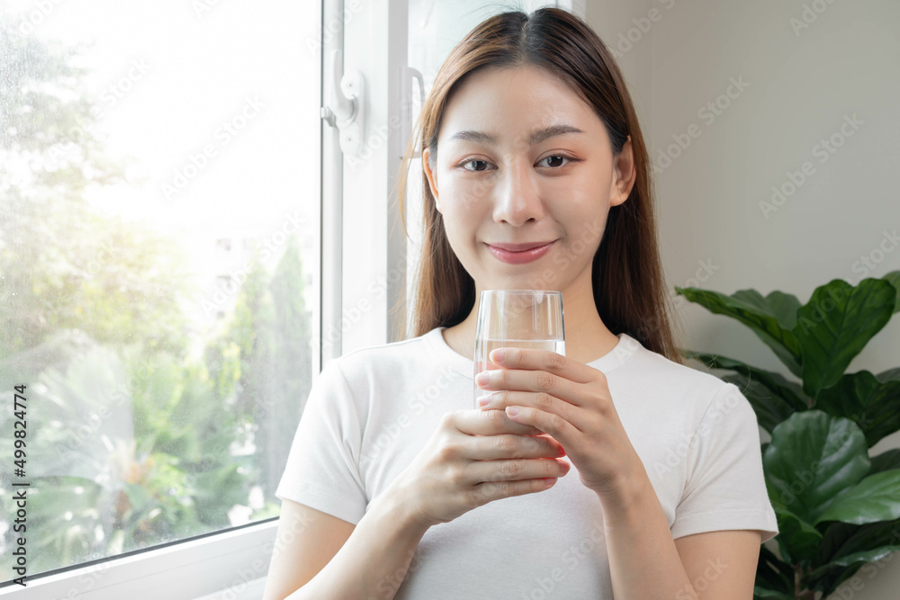 Happy beautiful, asian young woman, girl drinking, sip fresh glass of water for hydration of body, holding transparent glass in her hand, thirsty at home. Health care, healthy lifestyle concept. Happy beautiful, asian young woman, girl drinking, sip fresh glass of water for hydration of body, holding transparent glass in her hand, thirsty at home. Health care, healthy lifestyle concept.