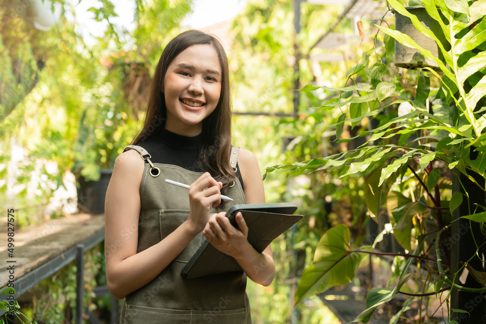 Asian female Woman gardener in apron working in a outdoor garden at home studio.Female Gardener using tablet computer for setting water drop system in greenhouse,modern greenhouse farm ideas concept Asian female Woman gardener in apron working in a outdoor garden at home studio.Female Gardener using tablet computer for setting water drop system in greenhouse,modern greenhouse farm ideas concept