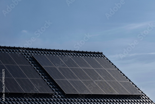 Solar panels mounted on the tile roof of a modern new-build house in the Netherlands with blue sky. Sustainable energy