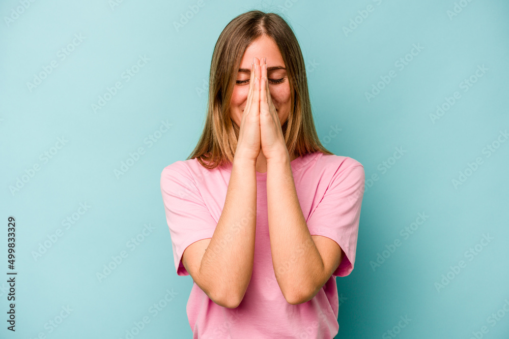 Young caucasian woman isolated on blue background holding hands in pray near mouth, feels confident. Young caucasian woman isolated on blue background holding hands in pray near mouth, feels confident.