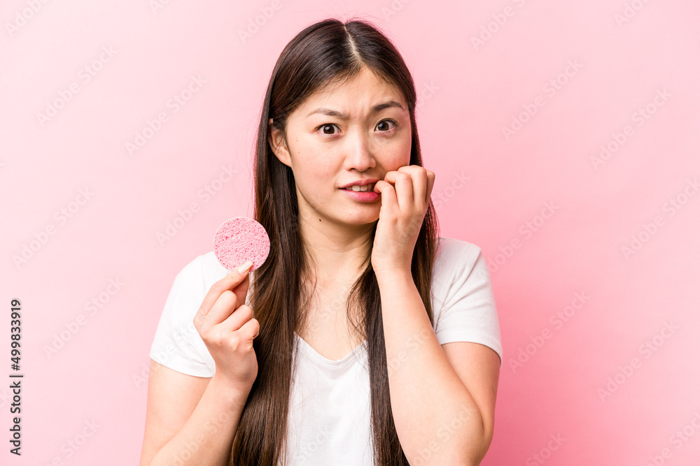 Young asian woman holding facial sponge isolated on pink background biting fingernails, nervous and very anxious. Young asian woman holding facial sponge isolated on pink background biting fingernails, nervous and very anxious.