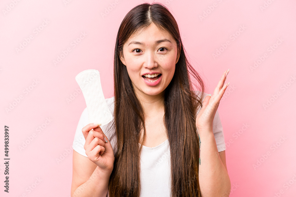 Young asian woman holding sanitary napkin isolated on pink background receiving a pleasant surprise, excited and raising hands. Young asian woman holding sanitary napkin isolated on pink background receiving a pleasant surprise, excited and raising hands.