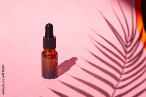 Bottle with dropper pipette with serum or essential oil. Pink background with daylight and beautiful palm shadows.Skincare products , natural cosmetic. Beauty concept for face and body care