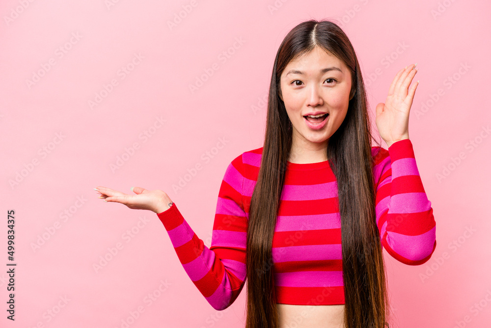 Young Chinese woman isolated on pink background holds copy space on a palm, keep hand over cheek. Amazed and delighted. Young Chinese woman isolated on pink background holds copy space on a palm, keep hand over cheek. Amazed and delighted.