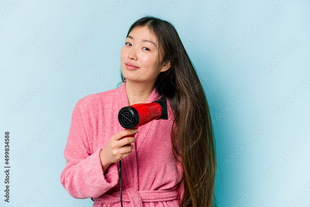 Young asian woman drying hair isolated on blue background Young asian woman drying hair isolated on blue background