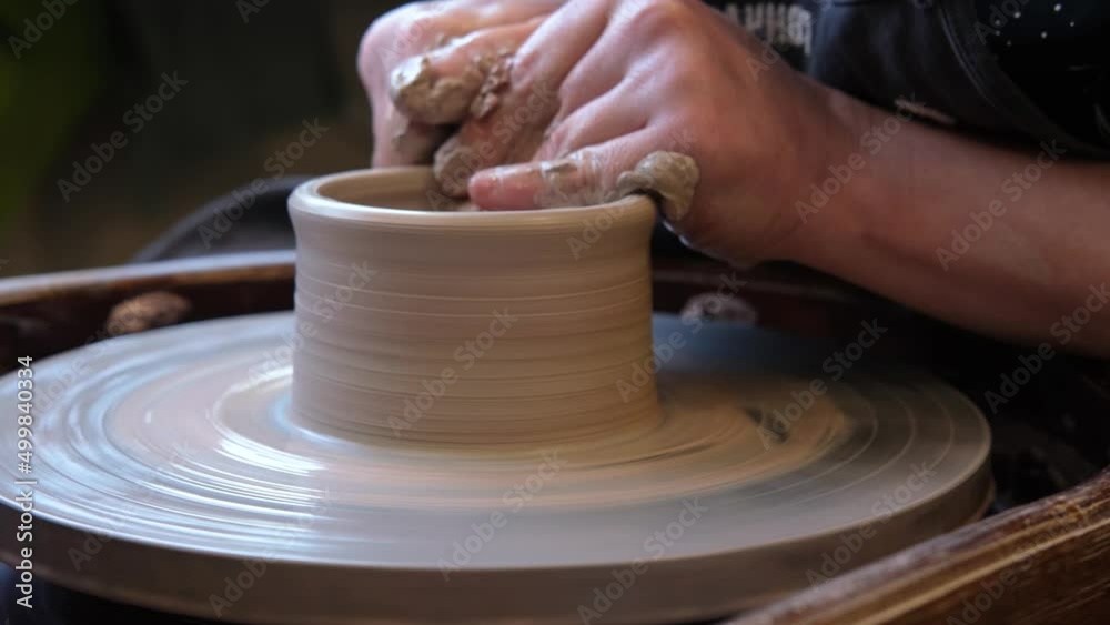 close up hand modeling pottery on a potter wheel in a cozy home workshop. Creating products from environmentally friendly clay with their own hands. Aesthetically beautiful female hands of the artist close up hand modeling pottery on a potter wheel in a cozy home workshop. Creating products from environmentally friendly clay with their own hands. Aesthetically beautiful female hands of the artist